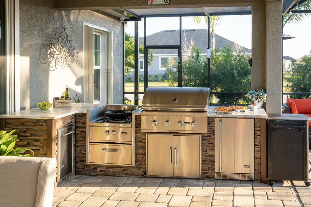 Outdoor kitchen on a Covered Patio with Stone Pavers, an Outdoor Stove, BBQ Grill, and a Fridge.